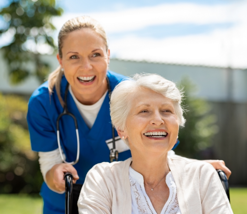Eine Pflegerin geht mit einer Seniorenheimbewohnerin im Garten spazieren